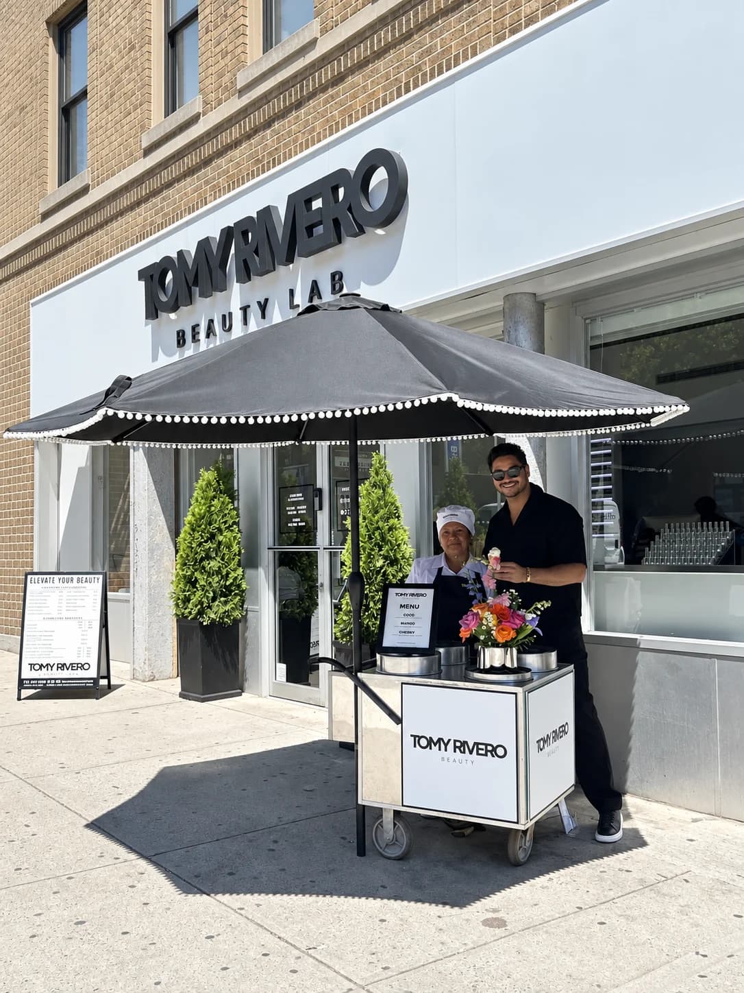 A Beauty Lab team member and colleague beside a flower cart outside the storefront