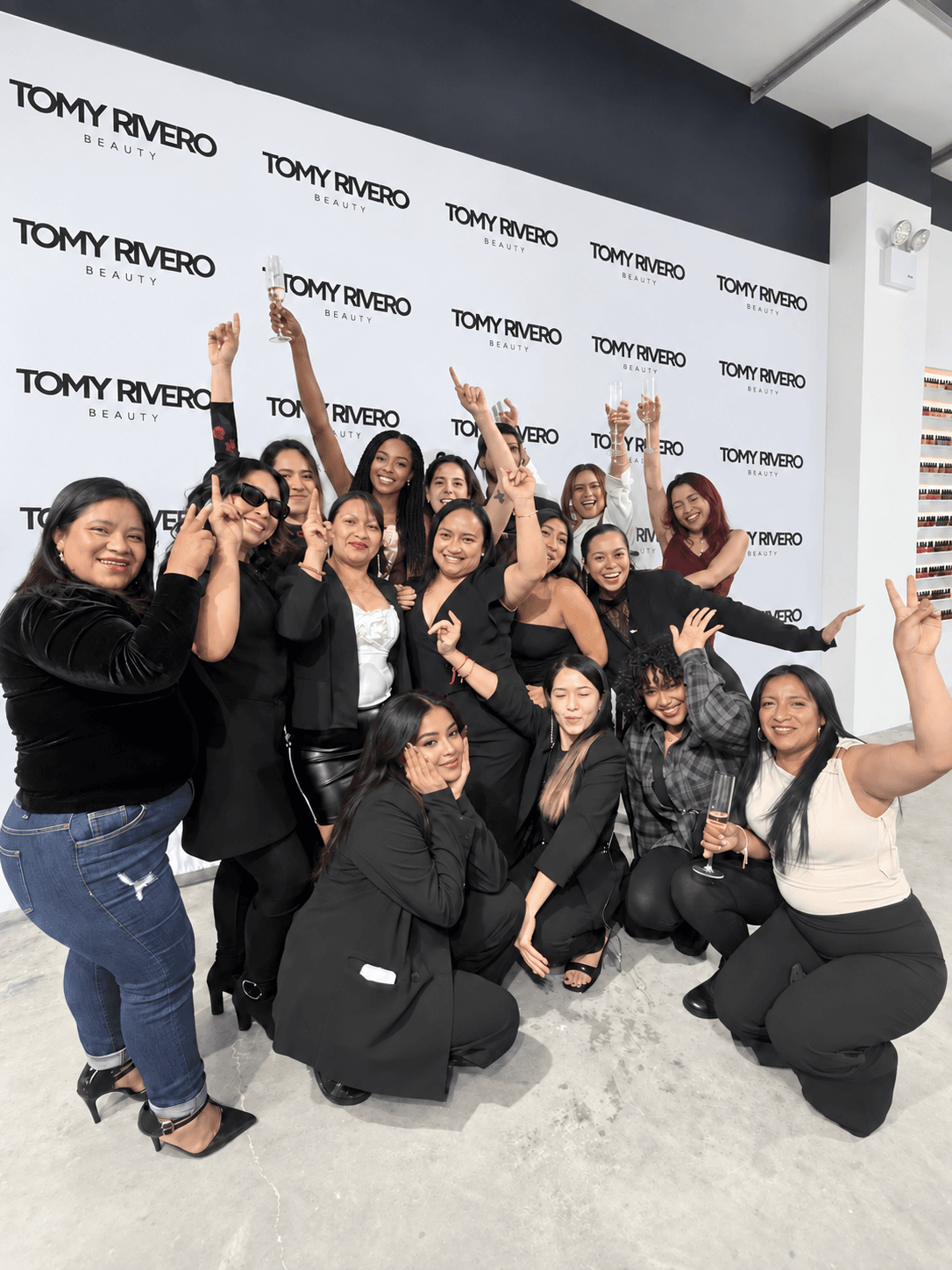 Tomy Rivero Beauty team celebrating together in front of a branded logo wall